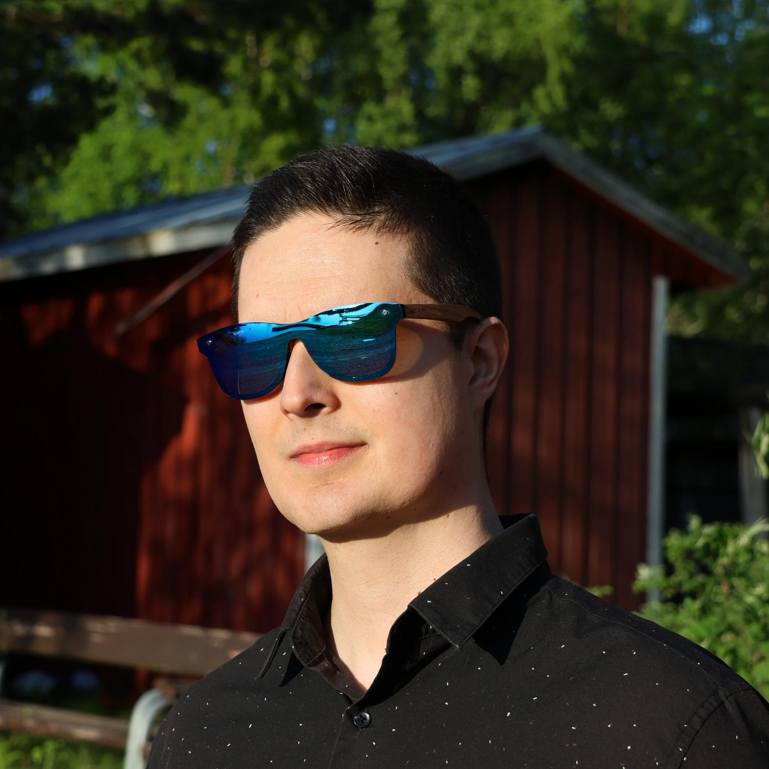 Korpi puusankaiset aurinkolasit sinisillä linssillä miehen päässä ulkona auringossa